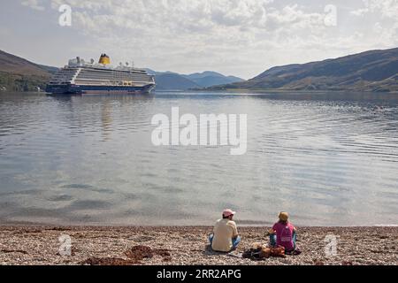 Ullapool, Highland, Écosse, Royaume-Uni. 6 septembre 2023. Brûlant dans les Highlands avec une température de 23 degrés centigrades à l'heure du déjeuner après un départ brumeux. Sur la photo : Toueists avec le paquebot Spirit of Adventure en arrière-plan. Couple se détendre sur la plage de galets avec le paquebot Spirit of Adventure en arrière-plan. Crédit : Scottishcreative/alamy Live News. Banque D'Images