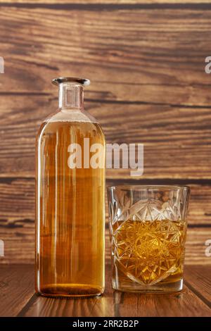 Une bouteille et un verre sculpté remplis d'une liqueur d'ambre entourés de surfaces en bois sombre Banque D'Images