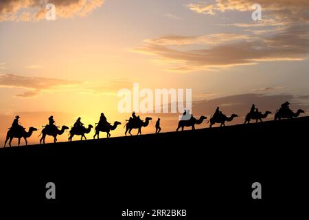 Lanzhou, province chinoise du Gansu. 15 juillet 2023. Les touristes montent à dos de chameau à la montagne Mingsha et au point pittoresque de Crescent Spring à Dunhuang, dans la province du Gansu du nord-ouest de la Chine, le 15 juillet 2023. Crédit : Zhang Xiaoliang/Xinhua/Alamy Live News Banque D'Images