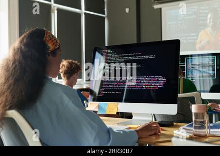 Vue arrière d'une écolière assise au bureau devant un écran d'ordinateur et travaillant avec des codes informatiques Banque D'Images