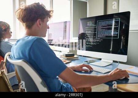 Vue arrière de l'étudiant assis au bureau avec ordinateur et codes de frappe pendant la leçon INFORMATIQUE Banque D'Images
