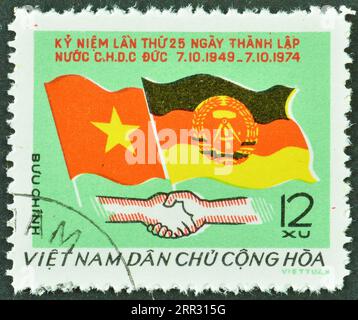 Timbre-poste annulé imprimé par le Vietnam qui montre drapeaux du Vietnam et de la République démocratique allemande, 25e anniversaire du Repub démocratique allemand Banque D'Images