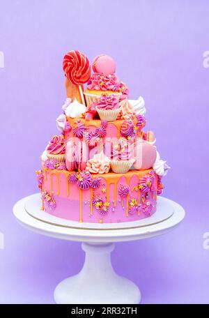 Gâteau dégradé rose, violet et orange avec des roses de fromage à la crème, macarons, cupcakes, meringues sur fond Uni violet Banque D'Images