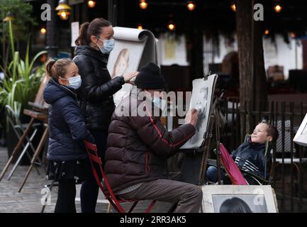 201029 -- PARIS, le 29 octobre 2020 -- Un artiste de rue dessine un portrait pour un garçon sur la place du Tertre à Montmartre, Paris, France, le 28 octobre 2020. La France entrera en confinement national à partir de vendredi pour endiguer la deuxième vague de l’épidémie de coronavirus, a annoncé mercredi soir le président Emmanuel Macron. La France a enregistré mercredi 36 437 nouvelles infections à COVID-19, 3 020 de plus que le nombre enregistré au cours des 24 heures précédentes. Le nombre cumulé de cas de coronavirus a grimpé à 1 235 132, dont 35 785 décès, en hausse de 244 en une journée, montrent les chiffres publiés par l’Agence de la santé publique Banque D'Images