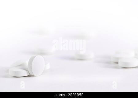 Pilules blanches en vrac reposent sur une table blanche, vue de face Blank pour l'espace de copie de conception. Banque D'Images