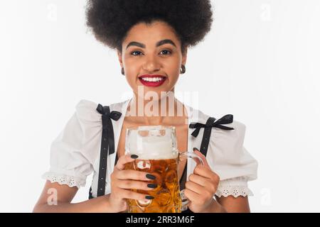 élégante serveuse afro-américaine oktoberfest avec tasse de bière artisanale souriant à la caméra sur blanc Banque D'Images