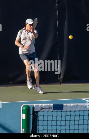 Un joueur masculin de pickleball retourne un service d'une balle jaune sur un terrain dédié dans un parc public. Banque D'Images