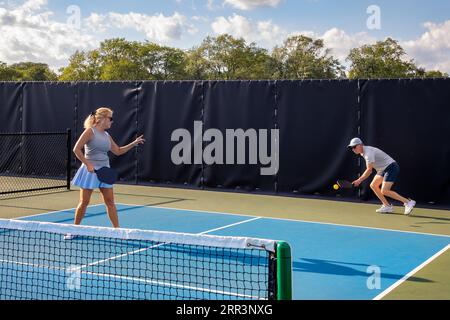 Un joueur de pickleball masculin renvoie une balle alors que sa partenaire féminine vérifie si la balle était dedans ou dehors. Banque D'Images