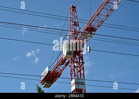 Une grue industrielle à tour de couleur rouge avec un bras tendu et une cabine de conducteur blanche vue derrière des câbles électriques. Banque D'Images