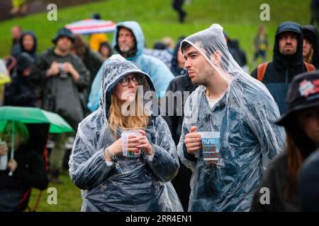 Un couple dans Wets avec des bières dans l'arène principale Mountain Stage dans la pluie et la boue de pluie. Green Man Festival, Brecon, pays de Galles, Royaume-Uni, 2023. Photo : Rob W. Banque D'Images