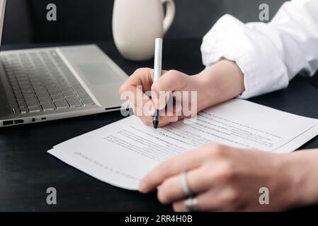 Une jeune femme signe un document officiel, une main de femme avec un stylo signe un contrat en papier. Affaires, avocat, finance, notaire, commerce, crédit Banque D'Images