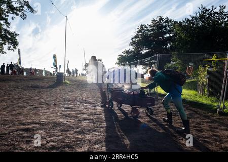 Un couple avec un chariot poussette lutte pour le pousser sur une colline boueuse au Green Man Festival, Brecon, pays de Galles, Royaume-Uni, 2023. Photo : Rob Watkins Banque D'Images