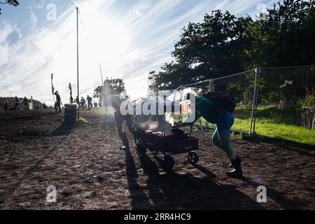 Un couple avec un chariot poussette lutte pour le pousser sur une colline boueuse au Green Man Festival, Brecon, pays de Galles, Royaume-Uni, 2023. Photo : Rob Watkins Banque D'Images