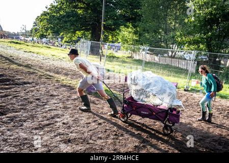 Un couple avec un chariot pousseur lutte pour le pousser jusqu'à une colline boueuse au Green Man Festival, Brecon, pays de Galles, Royaume-Uni, 2023. Photo : Rob Watkins Banque D'Images