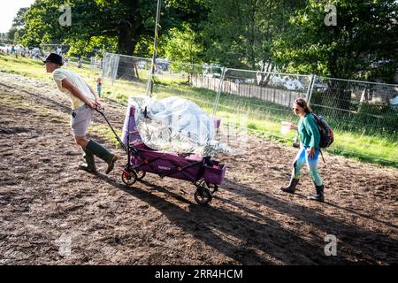 Un couple avec un chariot pousseur lutte pour le pousser jusqu'à une colline boueuse au Green Man Festival, Brecon, pays de Galles, Royaume-Uni, 2023. Photo : Rob Watkins Banque D'Images