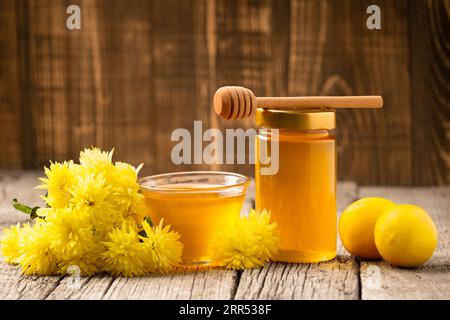 Miel de fleur dans un bocal en verre et un bol, godet en bois, citrons frais sur un fond en bois. Produits qui renforcent le système immunitaire. Banque D'Images