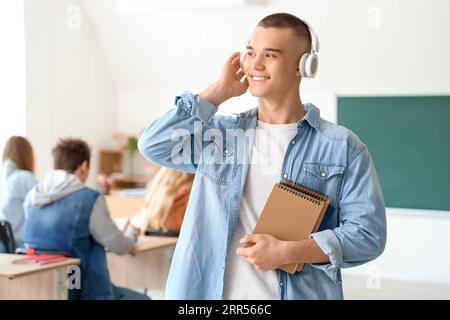 Étudiant masculin avec des cahiers écoutant de la musique en classe Banque D'Images