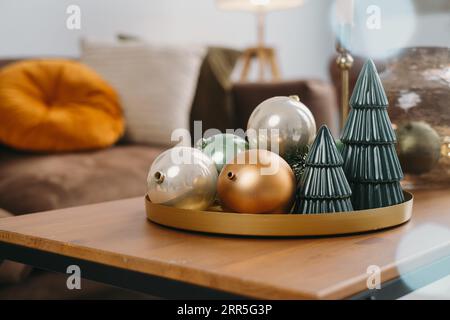 Décor de Noël sur la table du salon. Boules et petits arbres de jouet de Noël sur plateau par canapé en couleur dorée et verte. Intérieur de la chambre du nouvel an Banque D'Images