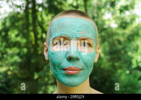 Une femme d'âge moyen dans un masque cosmétique repose sur le fond d'une forêt verte. Femme aux cheveux courts. Banque D'Images