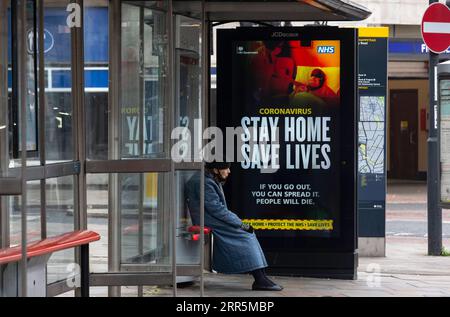 210110 -- LONDRES, le 10 janvier 2021 -- Une personne portant un masque facial est assise à côté d'un panneau publicitaire lisant Stay Home Save Lives à un arrêt de bus à Londres, en Grande-Bretagne, le 10 janvier 2021. Les décès liés au coronavirus en Grande-Bretagne ont dépassé 80 000 samedi avec 1 035 autres signalés dans le pays. BRETAGNE-LONDRES-COVID-19-CAS HanxYan PUBLICATIONxNOTxINxCHN Banque D'Images