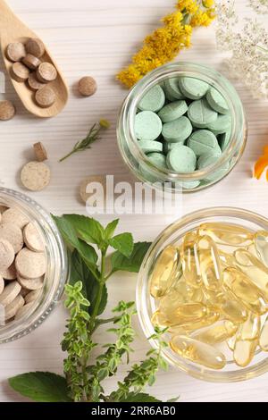 Différentes pilules, fleurs et herbes sur la table en bois blanc, pose à plat. Compléments alimentaires Banque D'Images