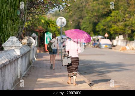 Une vue arrière d'une jeune fille laotienne en vêtements traditionnels et une fille européenne en vêtements décontractés se promène dans la rue dans la ville de Luang Prabang, Laos. Banque D'Images