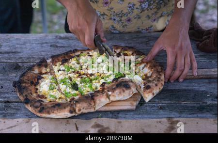 Plan rapproché d'une pizza fraîchement préparée découpée sur une planche de bois Banque D'Images