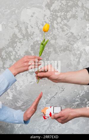 La main de la femme acceptant la tulipe jaune rejetant la cigarette de poche de l'homme Banque D'Images