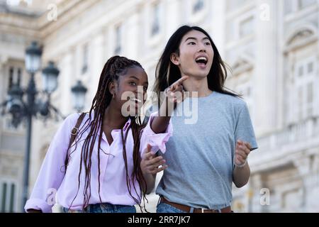 Jeune jeune couple multi-ethnique explorant la ville excitée de Madrid en tant que touristes, femme pointant avec son doigt la voie à suivre Banque D'Images