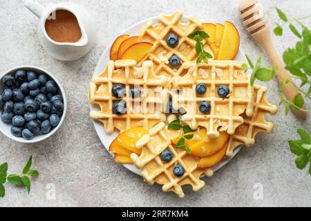 Gaufres fraîchement cuites avec des pêches et des bleuets sur un fond gris béton. Cuisson maison. Banque D'Images