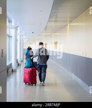 Couple poussant des sacs à bagages à l'aéroport, prêt à monter à bord du vol. Format vertical. Banque D'Images