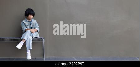 Fille enfant portant un costume de jeans bleu debout avec son amie en studio. Une fille triste regardant loin sur fond de mur gris dans la maison des parents de la famille Banque D'Images