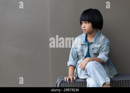 Fille enfant portant un costume de jeans bleu debout avec son amie en studio. Une fille triste regardant loin sur fond de mur gris dans la maison des parents de la famille Banque D'Images