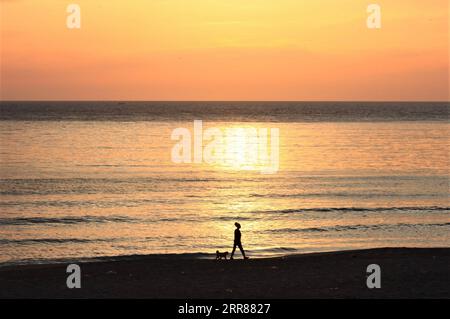 210423 -- BEYROUTH, le 23 avril 2021 -- Une femme promène un chien le long de la plage au coucher du soleil à Beyrouth, Liban, le 23 avril 2021. LIBAN-BEYROUTH-BORD DE MER-COUCHER DE SOLEIL LiuxZongya PUBLICATIONxNOTxINxCHN Banque D'Images