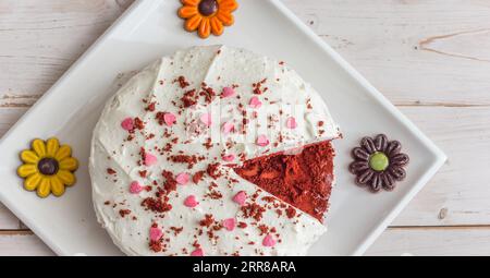 Vue panoramique d'un gâteau de velours rouge décoré de petits coeurs et de fleurs de chocolat sur une table en bois blanc Banque D'Images