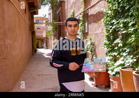 210514 -- KASHGAR, le 14 mai 2021 -- Mamattursunjian Mamatimen pose dans une ruelle de l'ancienne ville de Kashgar, dans la région autonome ouïgoure du Xinjiang, au nord-ouest de la Chine, le 8 mai 2021. La couleur dominante des habitations de l'ancienne ville de Kashgar dans le Xinjiang est le jaune foncé. Mais dans les œuvres du peintre local de 26 ans Mamattursunjian Mamatimen, plus de couleurs comme l'orange, le blanc, le violet, le bleu... sont utilisés pour peindre la ville. C'est son sentiment de vie, et aussi un sentiment partagé par les jeunes de Kashgar, a déclaré Mamattursunjian. Il faut du courage pour briser la tradition. Mamattursunjian a dit, quand je l'ai fait Banque D'Images