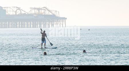 Brighton Royaume-Uni 7 septembre 2023 - Un paddle boarder et des nageurs à Brighton profitent d'un autre matin chaud et ensoleillé car les températures devraient atteindre à nouveau plus de 30 degrés dans certaines parties du Royaume-Uni : Credit Simon Dack / Alamy Live News Banque D'Images