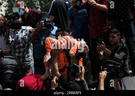 210516 -- GAZA, le 16 mai 2021 -- Un palestinien tient un enfant qui a été sauvé des décombres de maisons détruites à la suite de frappes aériennes israéliennes dans la rue Al-Wahda au milieu de la ville de Gaza, le 16 mai 2021. Les tensions entre Israël et les groupes militants dans la bande de Gaza se sont poursuivies dimanche pour le septième jour consécutif alors que le nombre de morts dans l'enclave côtière a grimpé à 181 et que 1 225 autres ont été blessés, ont déclaré des responsables. Le ministère de la Santé à Gaza a déclaré dans un communiqué de presse que depuis lundi, 181 Palestiniens ont été tués, dont 52 enfants et 31 femmes, et 1 225 autres ont eu des injuries différentes Banque D'Images