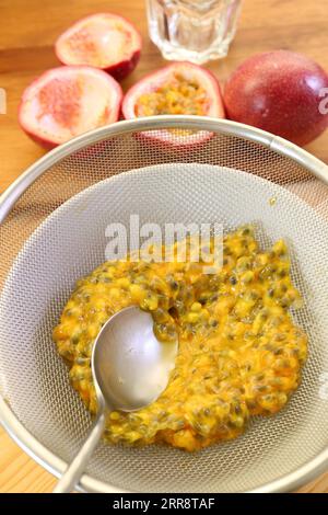 Une cuillère pinçant les pulpes de fruits de la passion sur un filtre pour extraire le liquide pour faire de la purée Banque D'Images