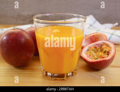 Verre de délicieux jus de fruits frais de la passion avec tas de fruits entiers en toile de fond Banque D'Images