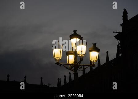 Lampe en fer forgé avec cinq lanternes éclairant faiblement avec une lumière jaune au crépuscule dans la place principale de Salamanque avec le ciel gris et dramatique et t Banque D'Images