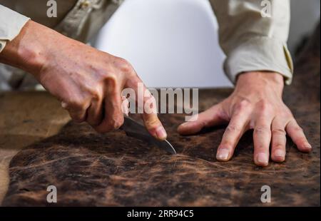 210527 -- XILINHOT, le 27 mai 2021 -- Xilinhu coupe le cuir dans son atelier de Xilinhot, dans la région autonome de Mongolie intérieure du nord de la Chine, le 26 mai 2021. L'équitation, le tir à l'arc et la lutte sont appelés les trois compétences des hommes du groupe ethnique mongol. Depuis 2005, l ' artisan Xilinhu du groupe ethnique mongol a intégré les symboles culturels de la selle, de l ' arc, de la flèche et du costume de lutte dans la fabrication d ' objets artisanaux pour promouvoir la culture traditionnelle du groupe ethnique. CHINE-INTÉRIEUR MONGOLIE-XILINHOT-ARTISANAT CN PENGXYUAN PUBLICATIONXNOTXINXCHN Banque D'Images