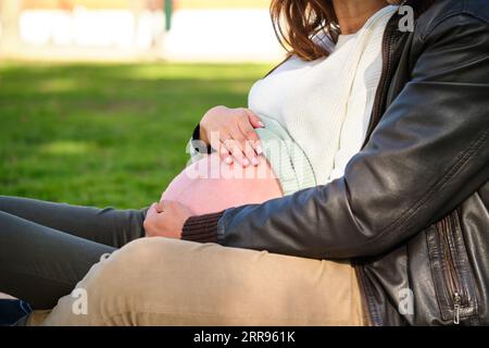 Un couple méconnaissable embrasse le ventre de sa femme enceinte dans un parc. Grossesse. Banque D'Images