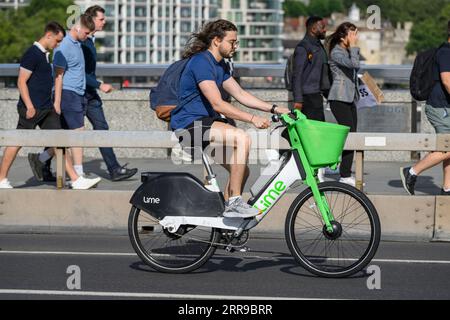 Un homme faisant la navette sur un vélo électrique Lime de location à travers pendant l'heure de pointe. , Londres, Royaume-Uni. 17 Jul 2023 Banque D'Images