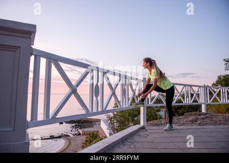 Jeune athlète nouant des lacets sur des baskets sur la chaussée au lever du soleil. Séance de remise en forme de pause, routine du matin. Gros plan portrait sportif de caucasien g Banque D'Images