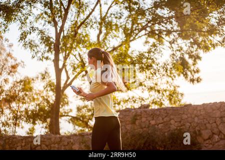 Portrait rapproché d'une jeune femme en vêtements de sport, jogging dans le parc au bord de la mer, tenue d'un smartphone, parlant au téléphone. Le concept de sport an Banque D'Images