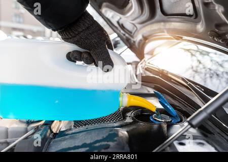 Gros plan de gants conducteur ou mécanicien versant du liquide antigel bleu pour le lavage de pare-brise de voiture d'hiver avec arrosoir bootle Banque D'Images