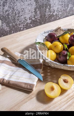 Un panier en osier peint en blanc avec quelques prunes jaunes mûres avec des prunes rouges et un couteau aiguisé pour les couper en deux Banque D'Images