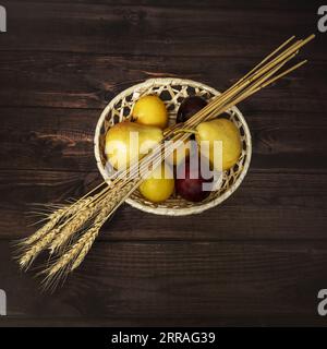 Une nature morte avec un panier rond en osier plein de fruits et quelques branches de blé Banque D'Images