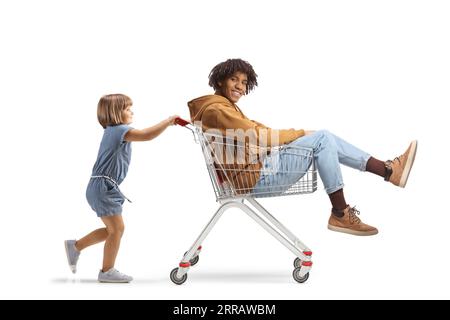 Petite fille caucasienne poussant un jeune homme afro-américain à l'intérieur d'un panier isolé sur fond blanc Banque D'Images